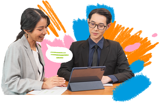 A man and a woman at a work desk, dressed in formal work attire while looking at a tablet.